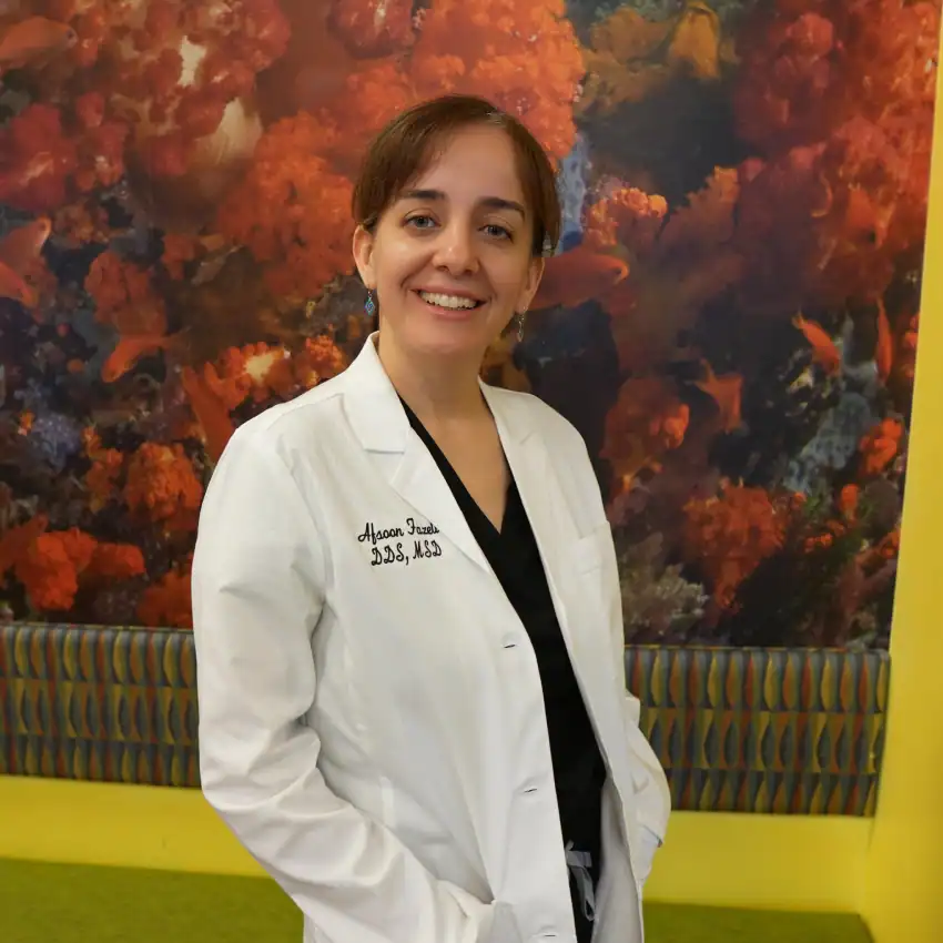 Dr. Fazeli of Discovery Children’s Dentistry smiling in a white lab coat indoors.